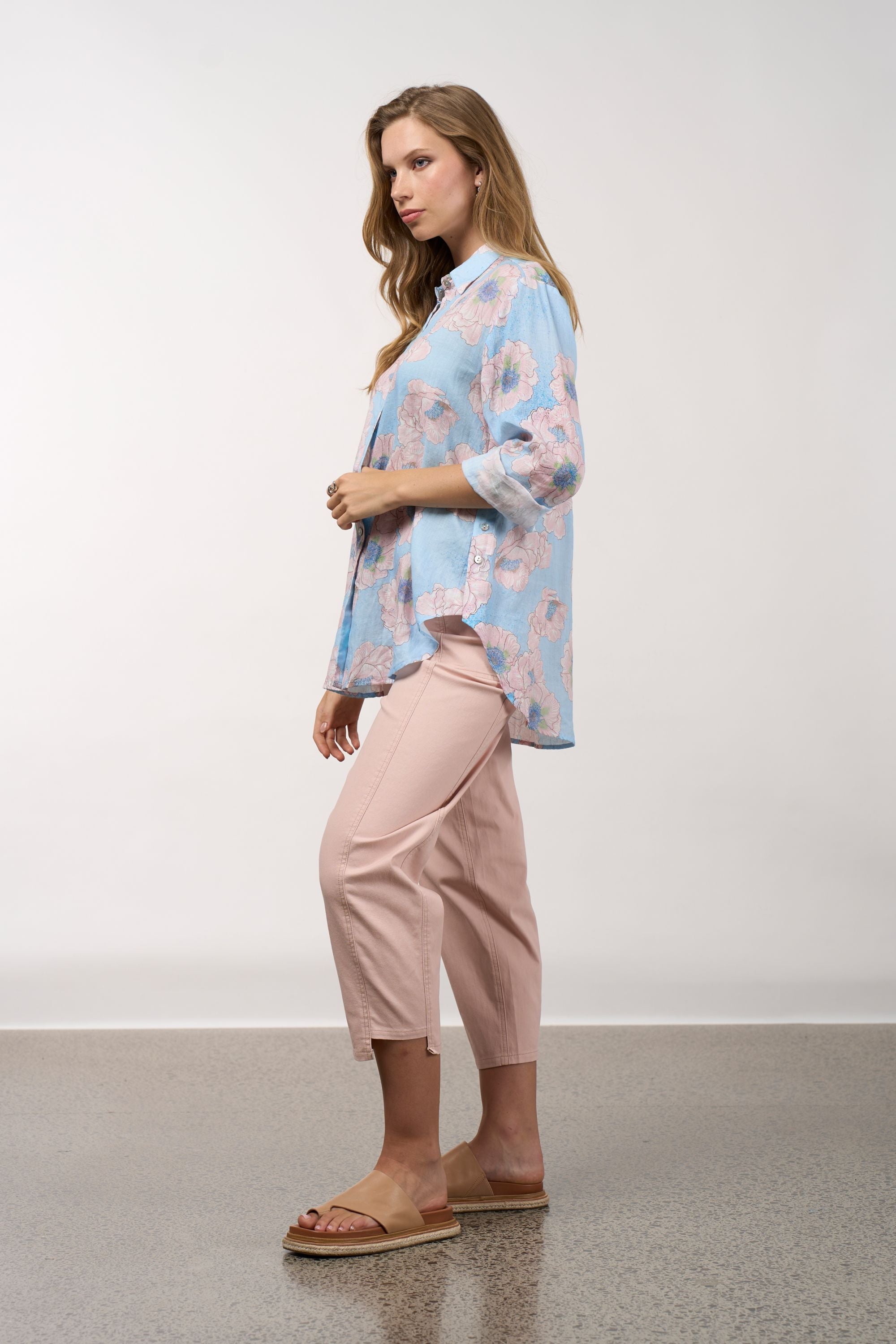 Woman wearing a light blue floral blouse and pink pants on a white background