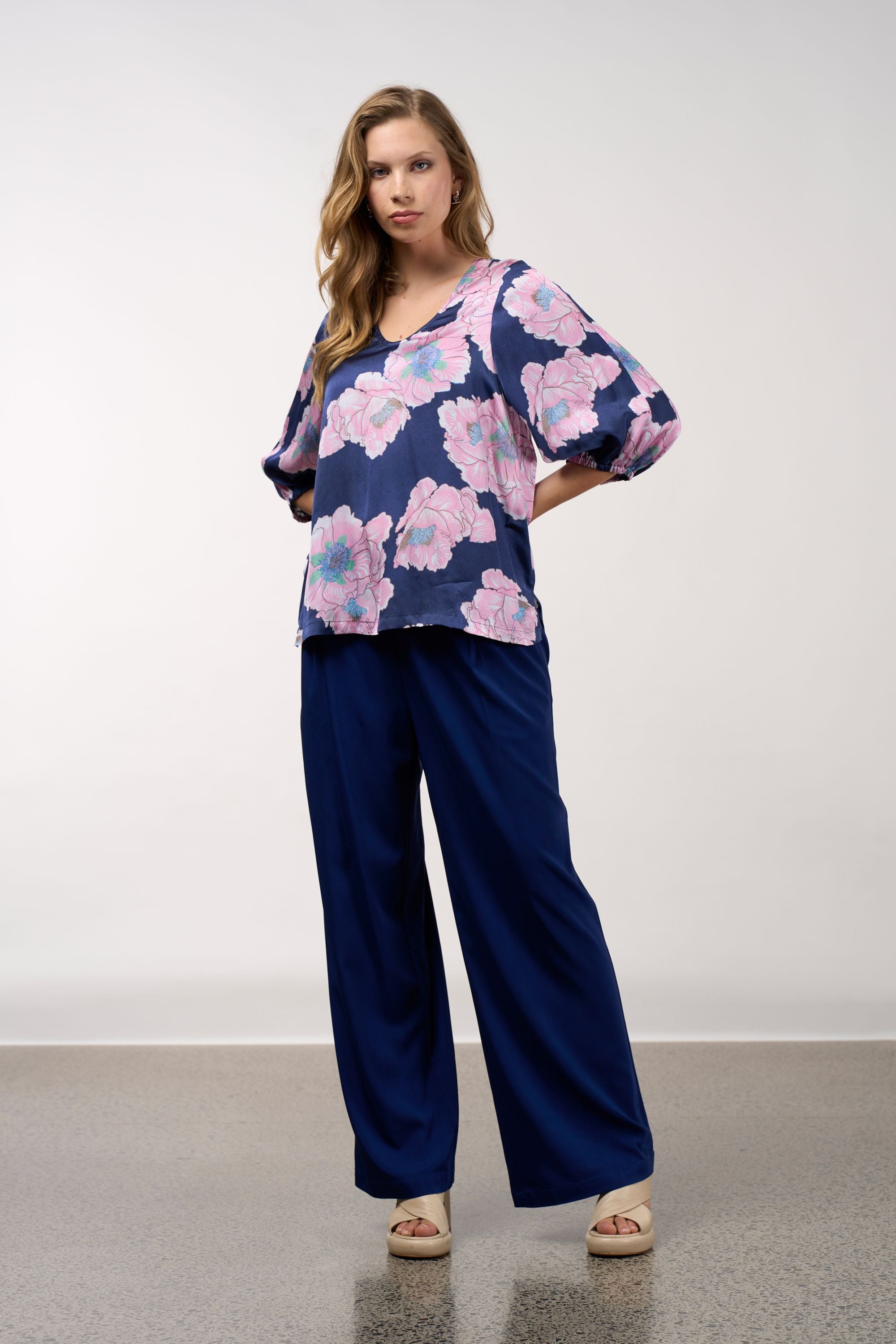 Woman wearing a floral top and navy pants against a white background