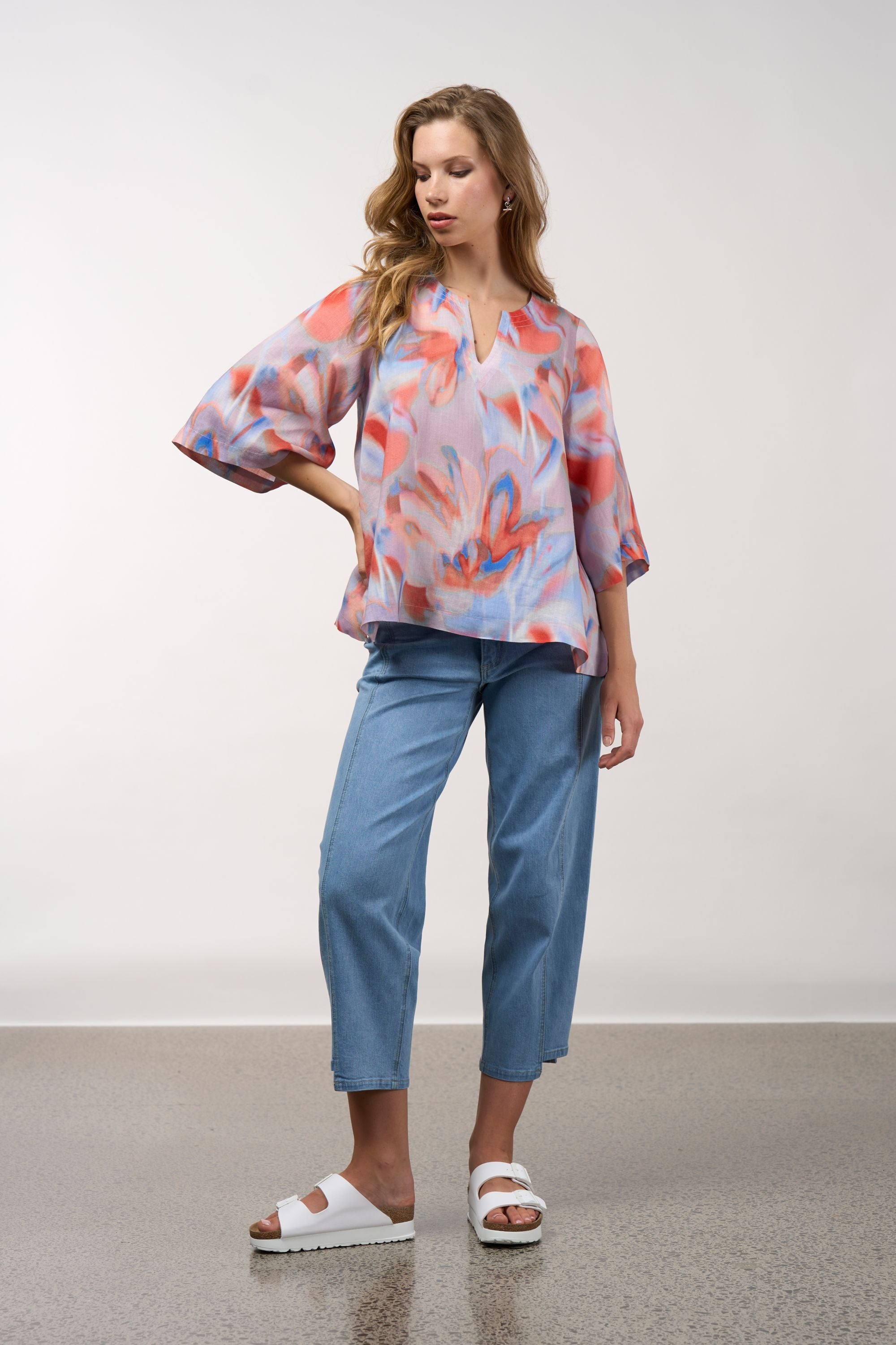 Woman wearing a colorful blouse and blue pants on a plain background