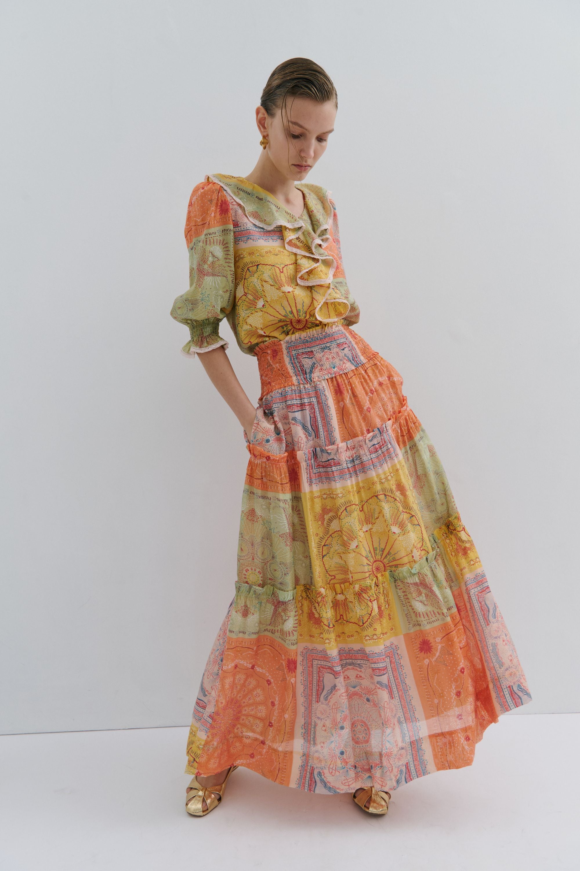 Woman wearing a colorful outfit with a patterned skirt and blouse on a white background