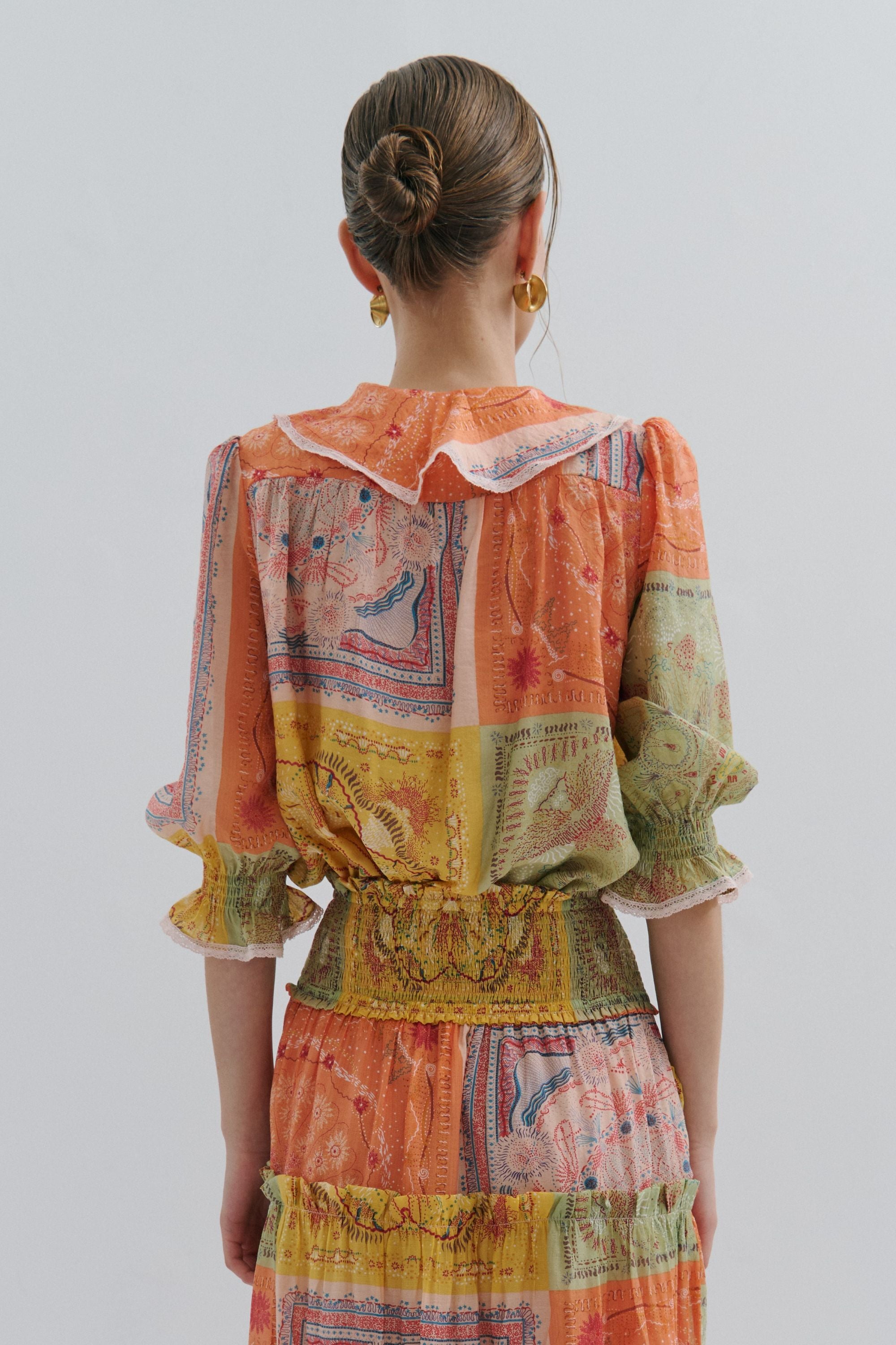 Woman wearing a colorful patchwork dress with a patterned blouse on a plain background