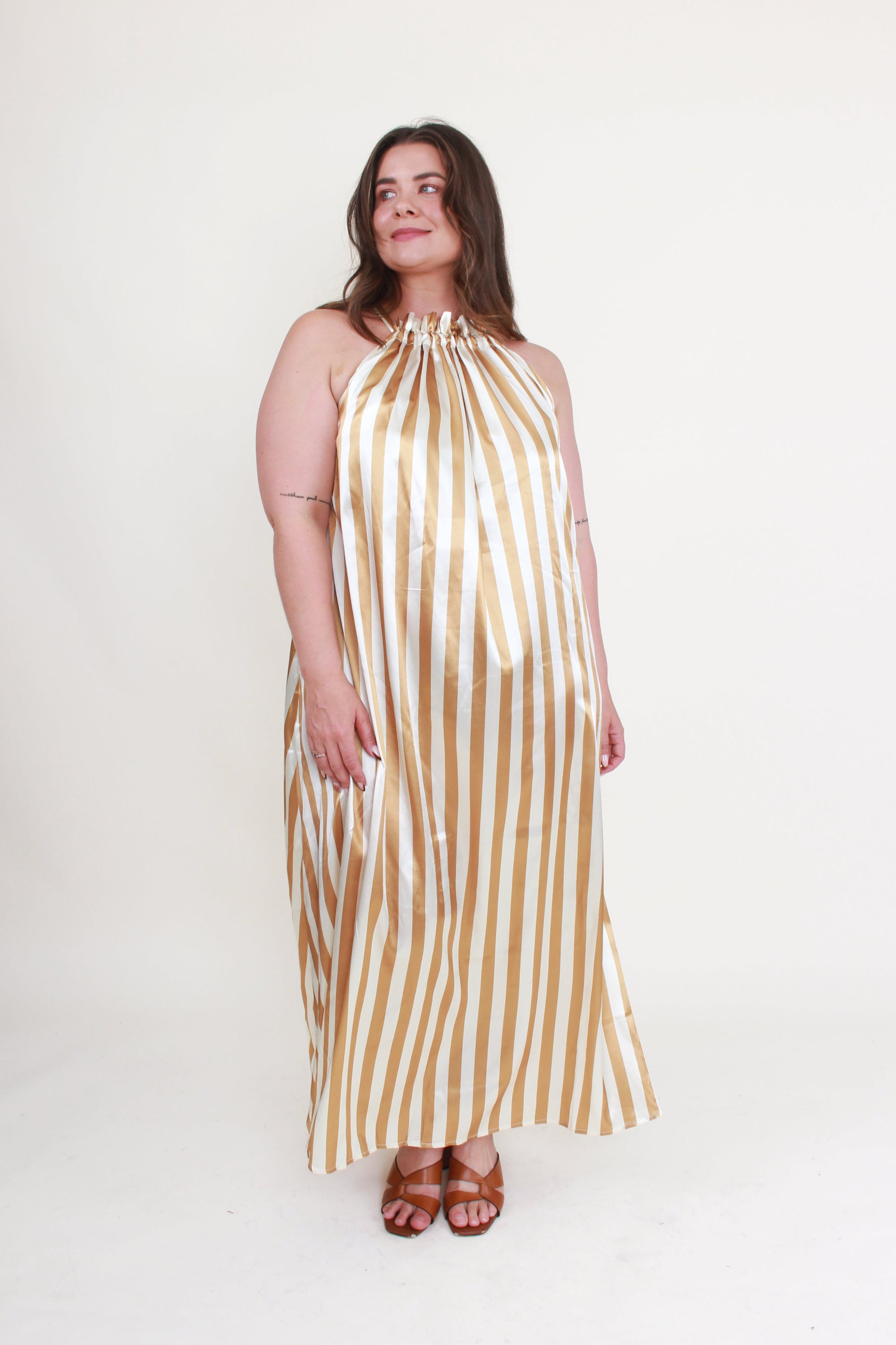 Woman wearing a gold and white striped dress on a white background