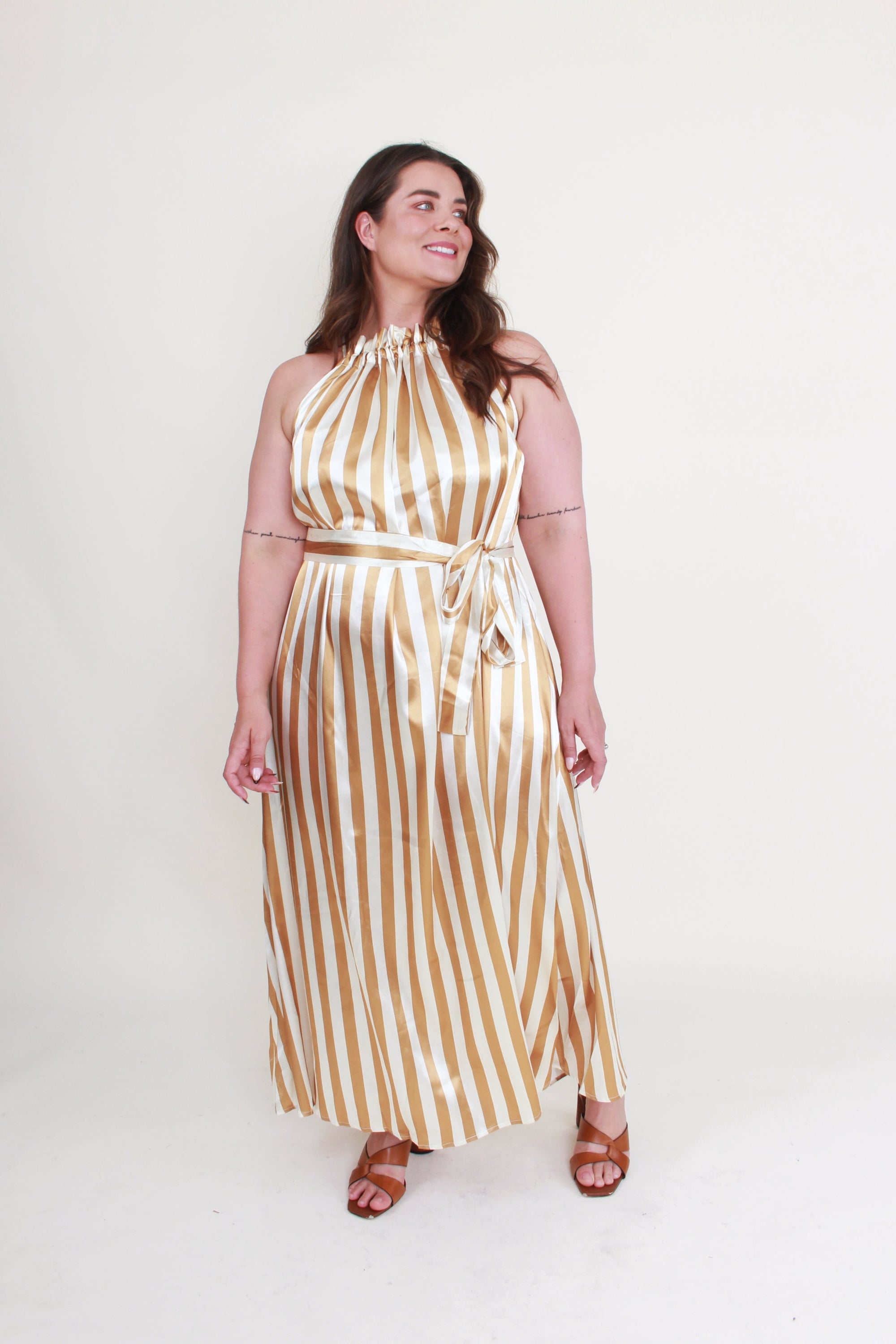 Woman wearing a gold and white striped dress on a white background