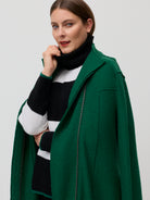 Woman wearing a green coat over a black and white striped sweater on a plain background