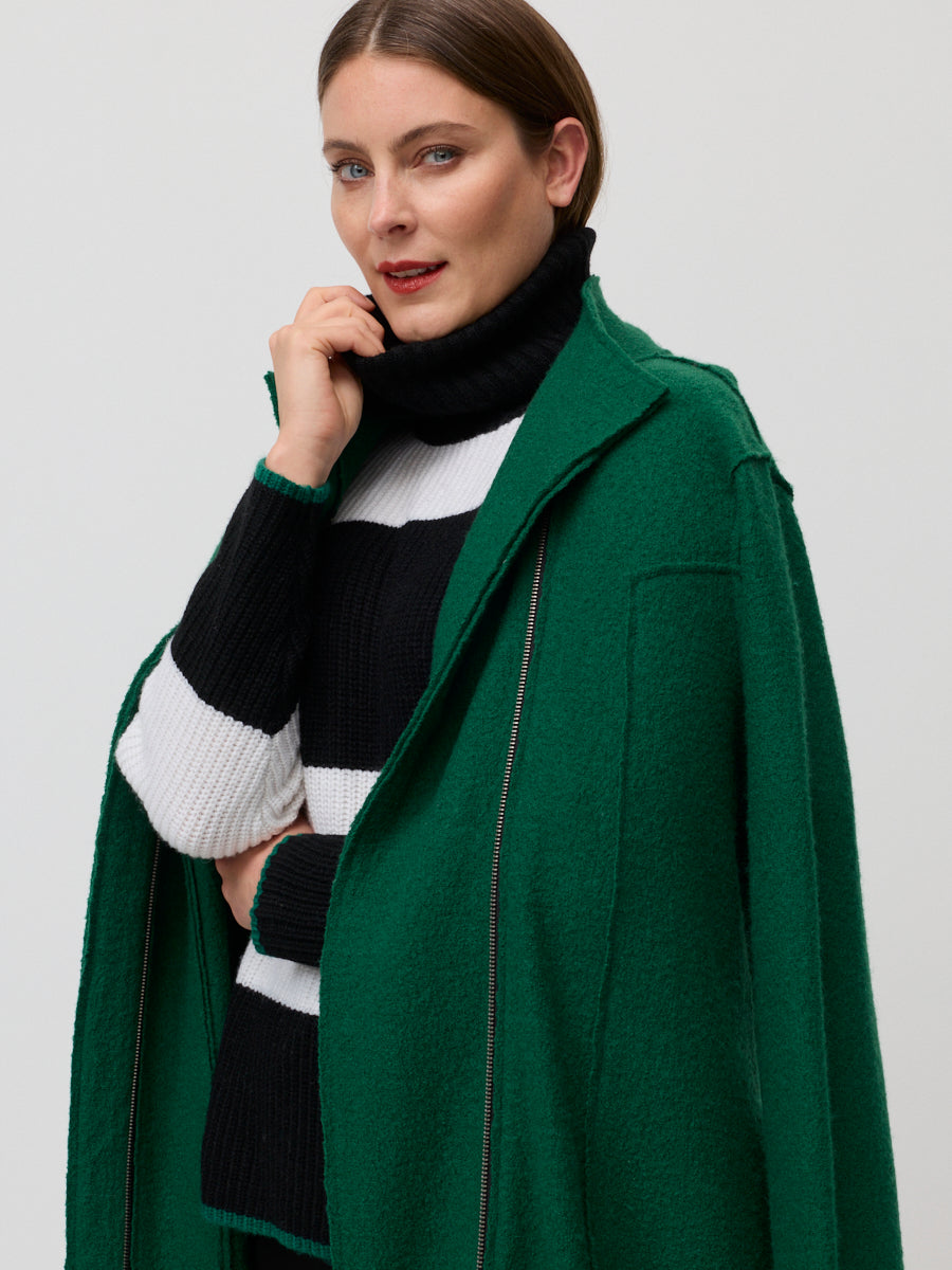 Woman wearing a green coat over a black and white striped sweater on a plain background