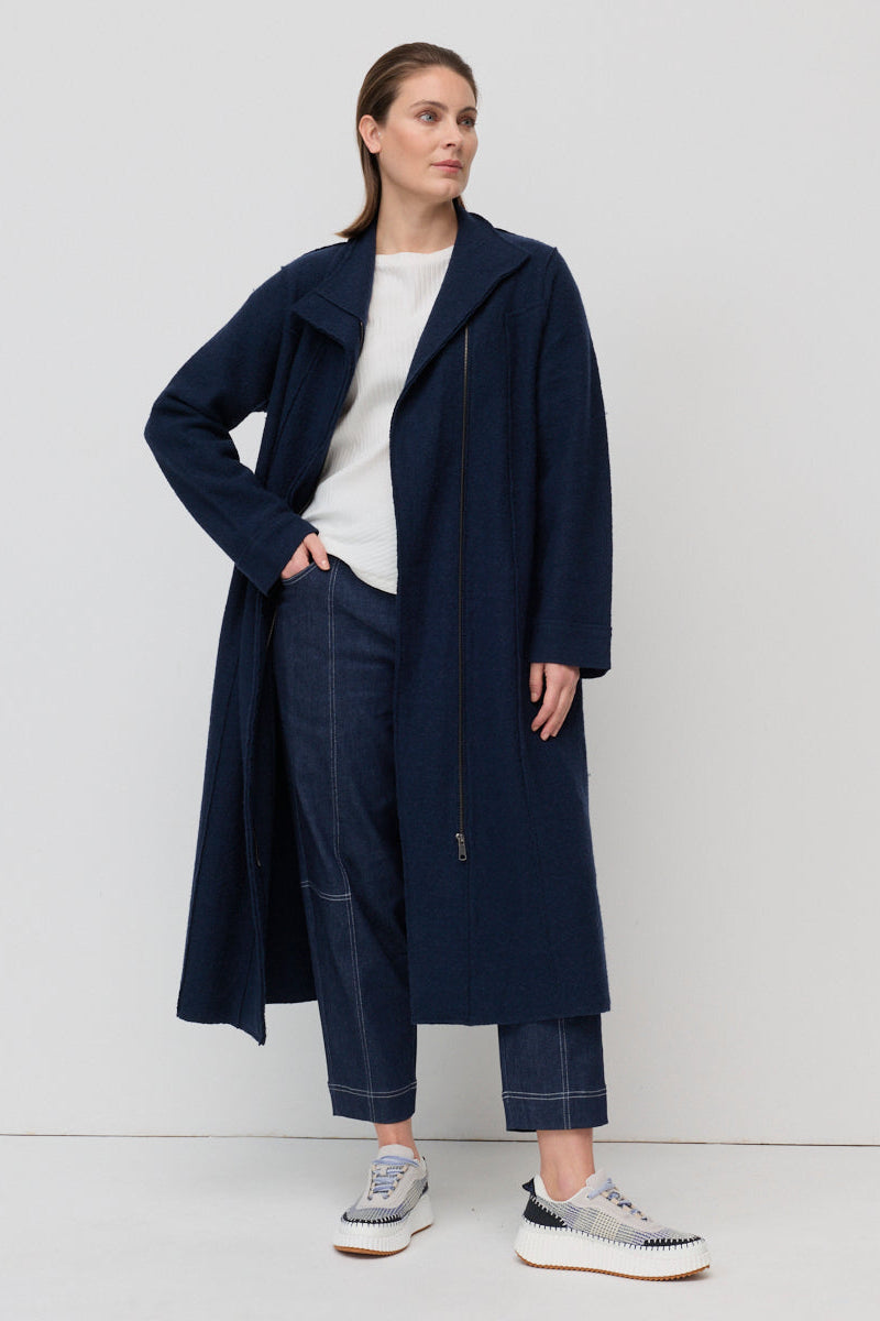 Woman wearing a navy coat and pants against a white background