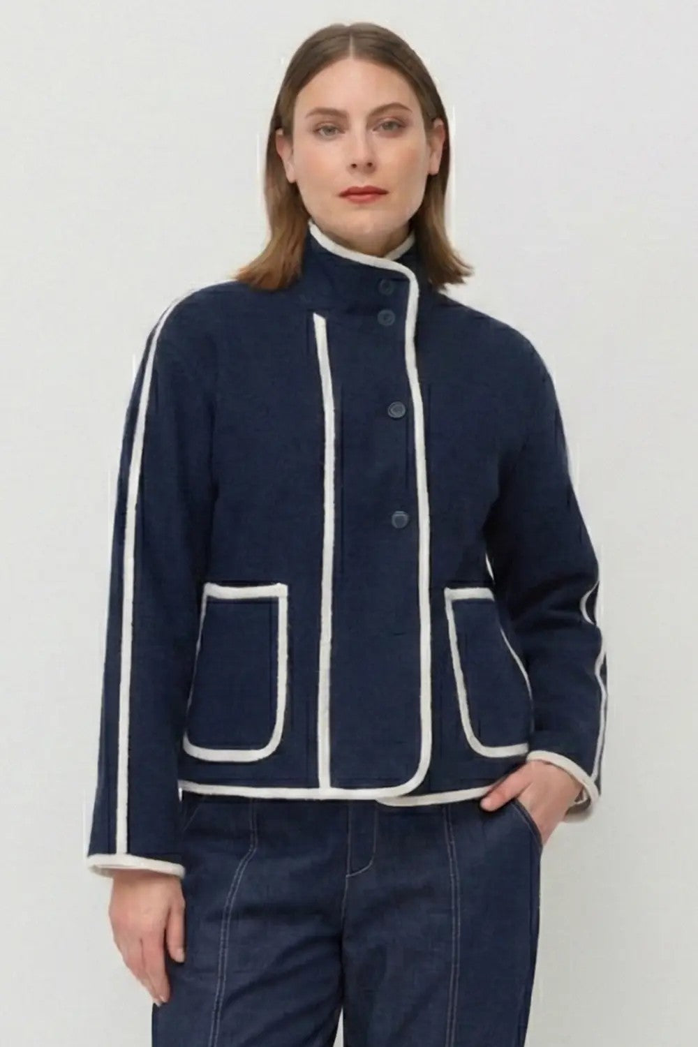 Person wearing a navy blue jacket with white trim on a plain background