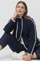 Woman wearing a navy coat with white trim sitting on a white floor.