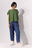 Woman wearing a green tee shirt and wide leg 7/8 light denim pants with contrast top stitching and pockets against a white background.