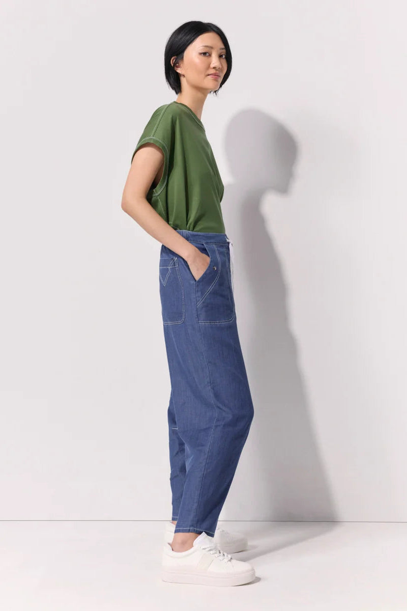 Woman wearing a green tee shirt and wide leg 7/8 light denim pants with contrast top stitching and pockets against a white background.