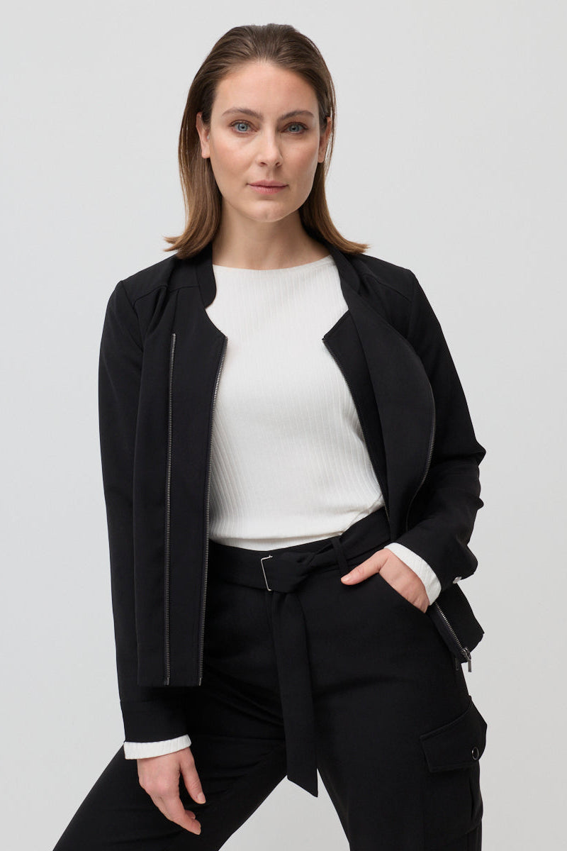 Woman wearing a black jacket over a white shirt and black pants on a light gray background