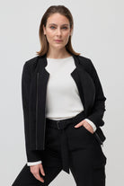 Woman wearing a black jacket over a white shirt and black pants on a light gray background