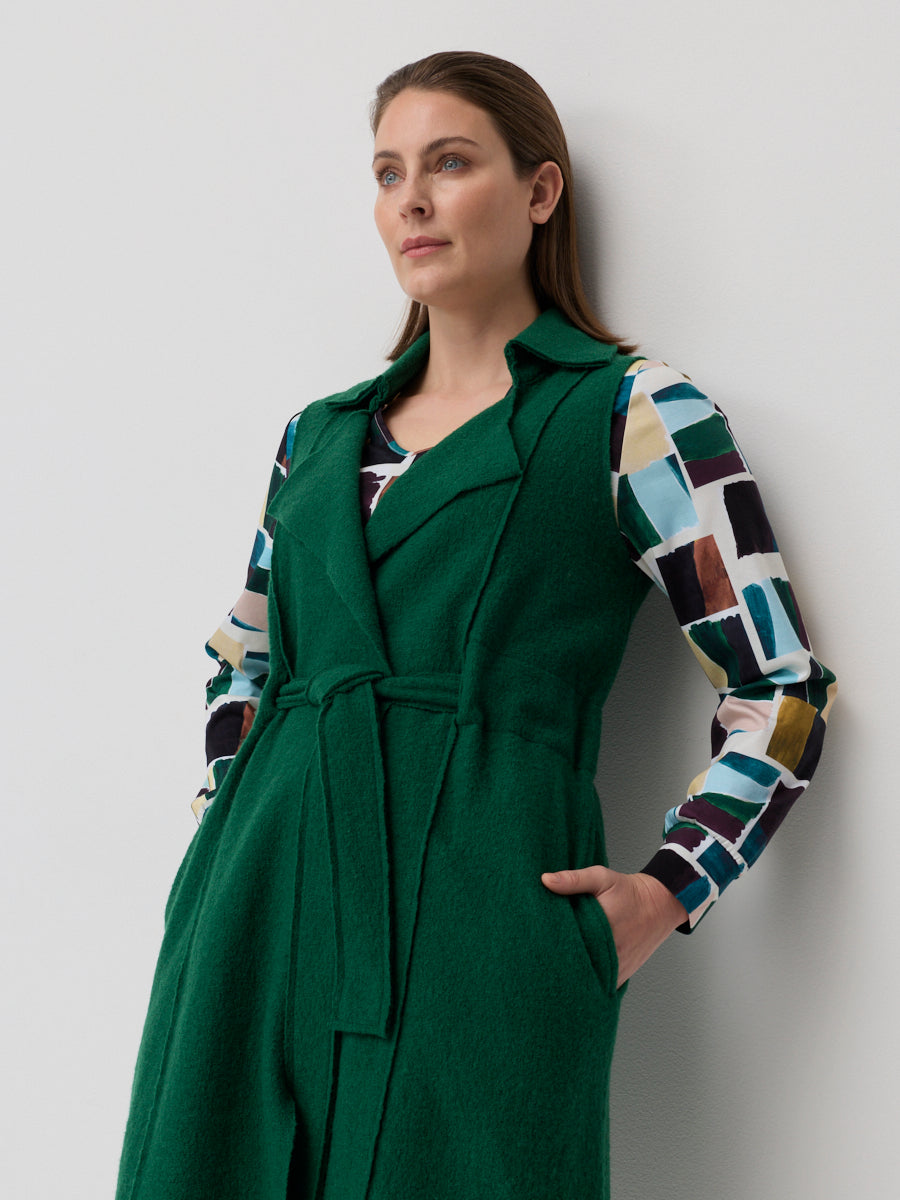 Woman wearing a green coat over a colorful patterned shirt against a plain background