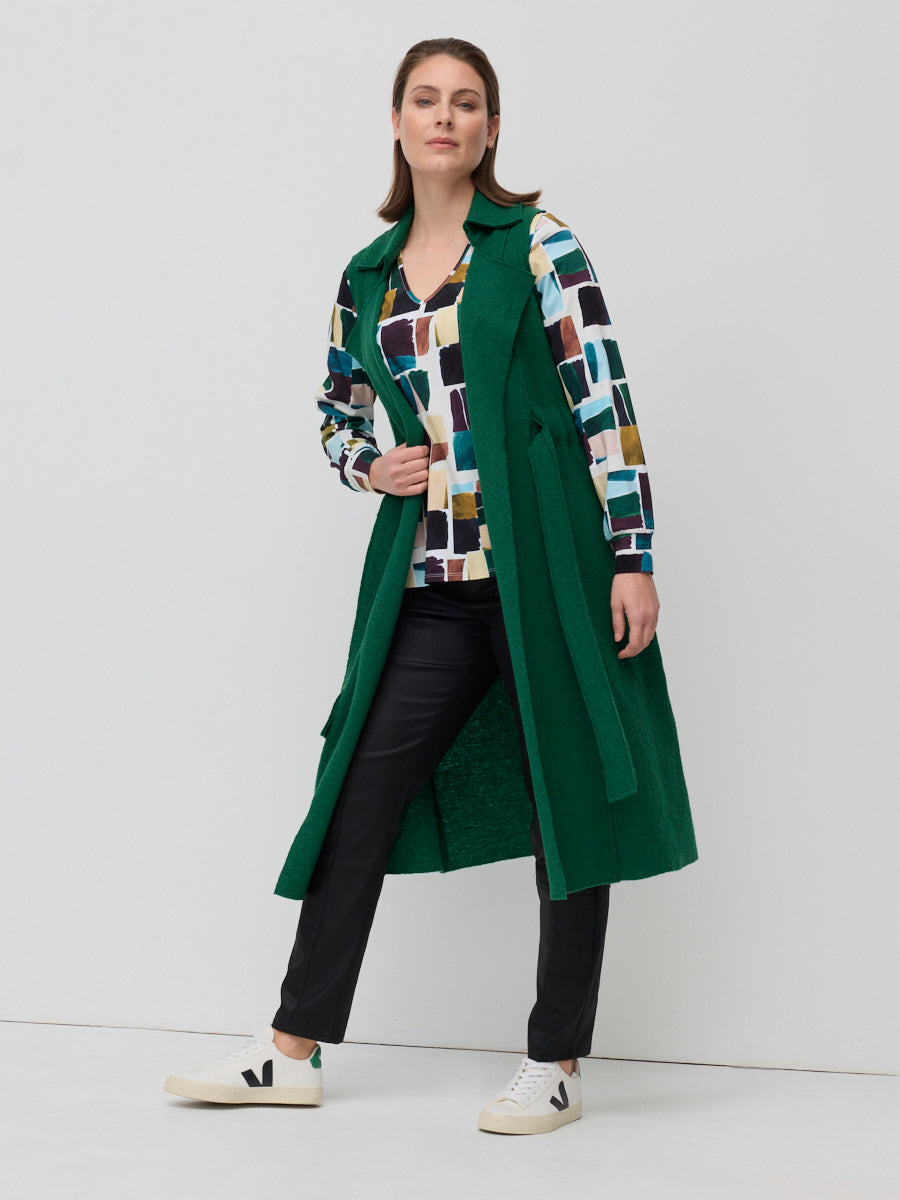 Woman wearing a green coat over a patterned shirt with a white background