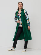Woman wearing a green coat over a patterned shirt with a white background