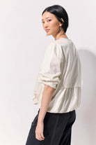 Woman wearing a cropped jacket with pushed up sleeves and no collar against a white background.