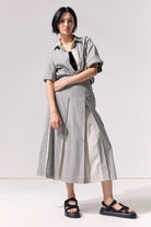 A woman wearing a pleated striped midi skirt and matching top against a white background.