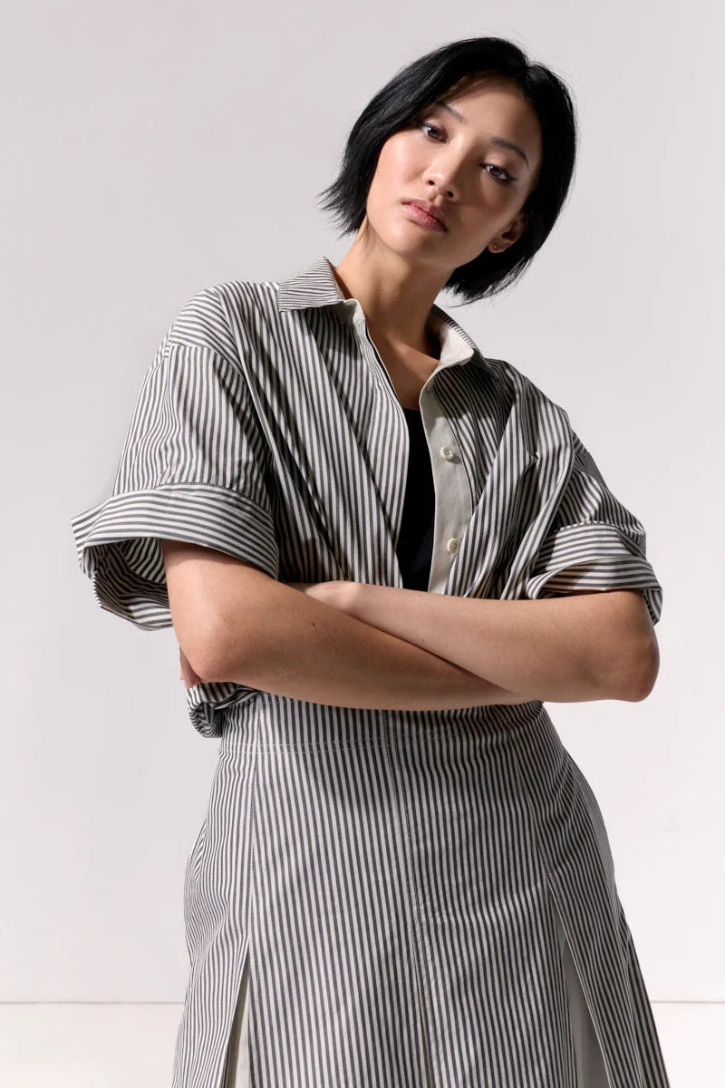 A woman wearing a pleated striped midi skirt and matching top against a white background.
