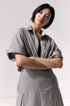 Woman wearing a striped overshirt with collar and cuffed sleeves against a white background.