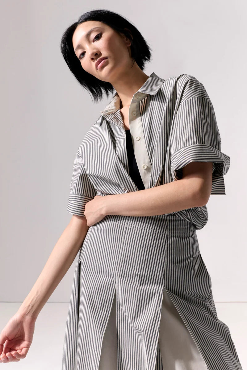 A woman wearing a pleated striped midi skirt and matching top against a white background.