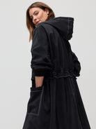 Woman wearing a black hooded coat on a light gray background