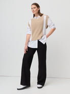 Woman wearing a beige vest over a white shirt with black pants on a white background