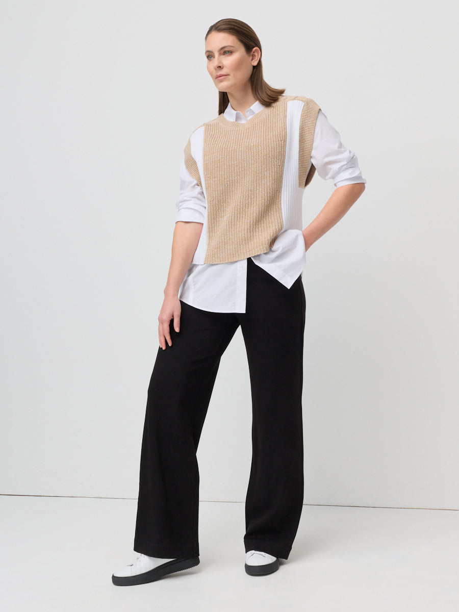 Woman wearing a beige vest over a white shirt with black pants on a white background
