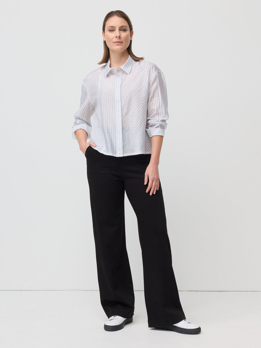 Woman wearing a white blouse with black patterns and black pants on a white background