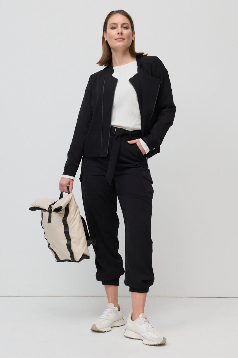 Woman wearing a black outfit with a white top, holding a black and white bag on a white background