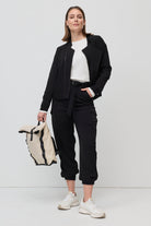 Woman wearing a black outfit with a white top, holding a black and white bag on a white background