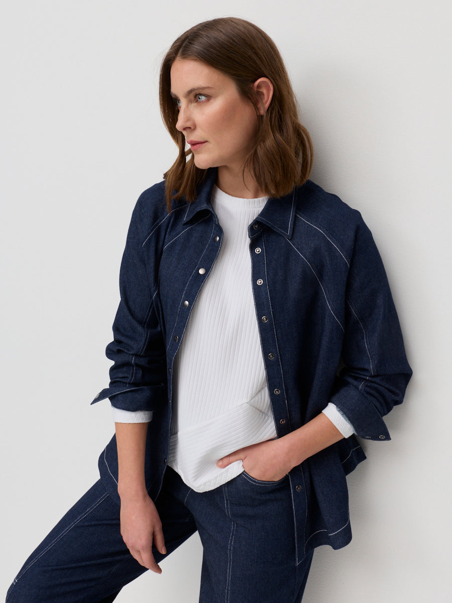 Woman wearing a navy denim jacket over a white shirt against a light gray background