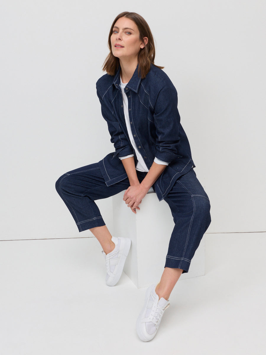 Woman wearing a navy denim outfit sitting on a white surface