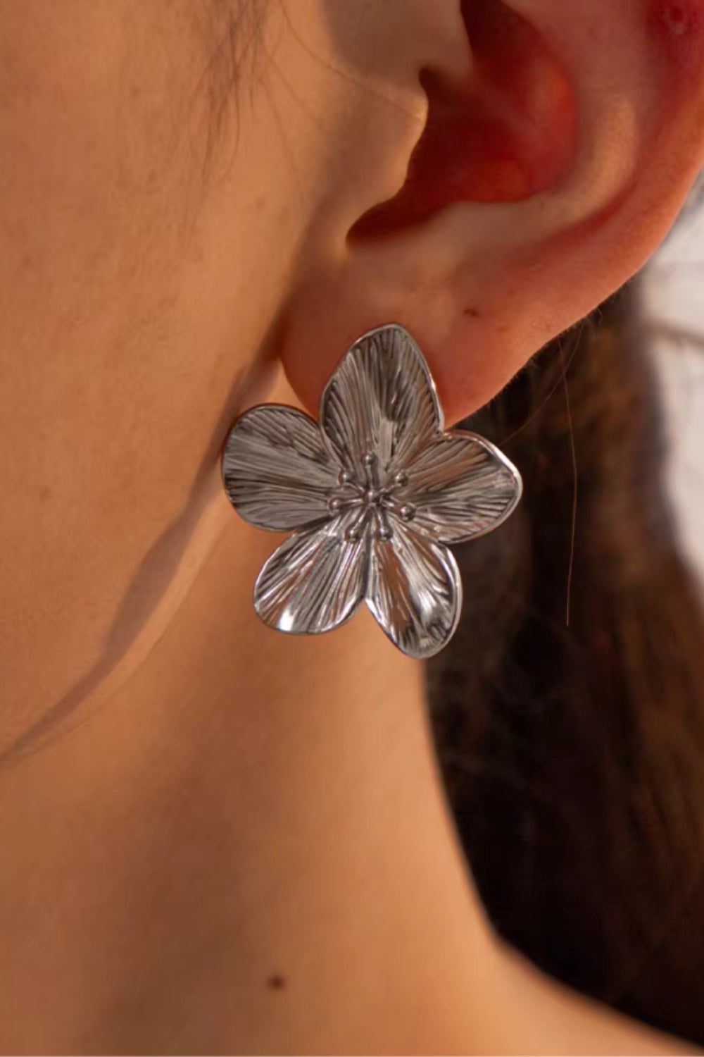 Silver flower-shaped earring worn on an ear with a blurred background