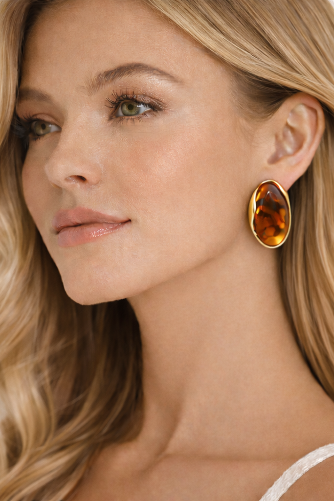 Woman wearing a gold earring with a amber stone on a neutral background