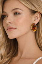 Woman wearing a gold earring with a amber stone on a neutral background