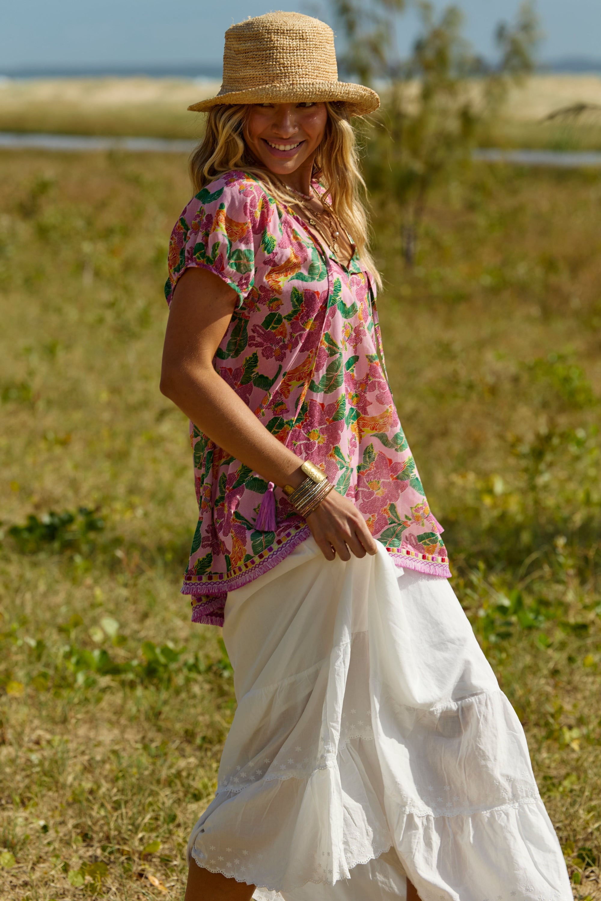 Woman in a colorful top and white skirt standing in a grassy field.