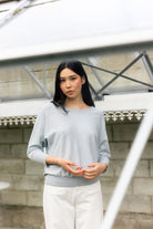 Woman wearing a light gray sweater and white pants standing outdoors.