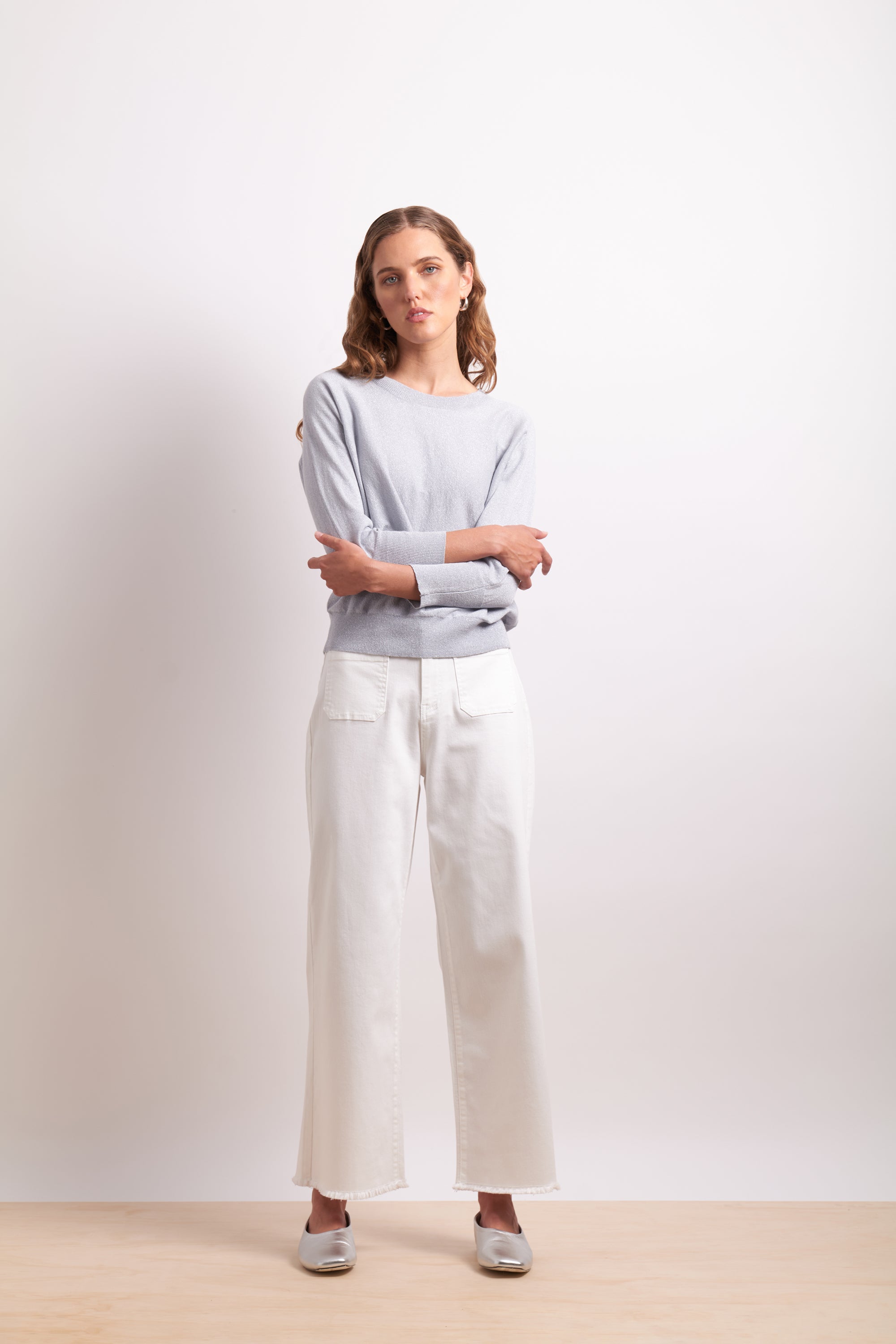 Woman wearing a light gray sweater and white pants on a plain background