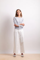 Woman wearing a light gray sweater and white pants on a plain background