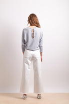 Person wearing a light gray sweater and white pants on a plain background