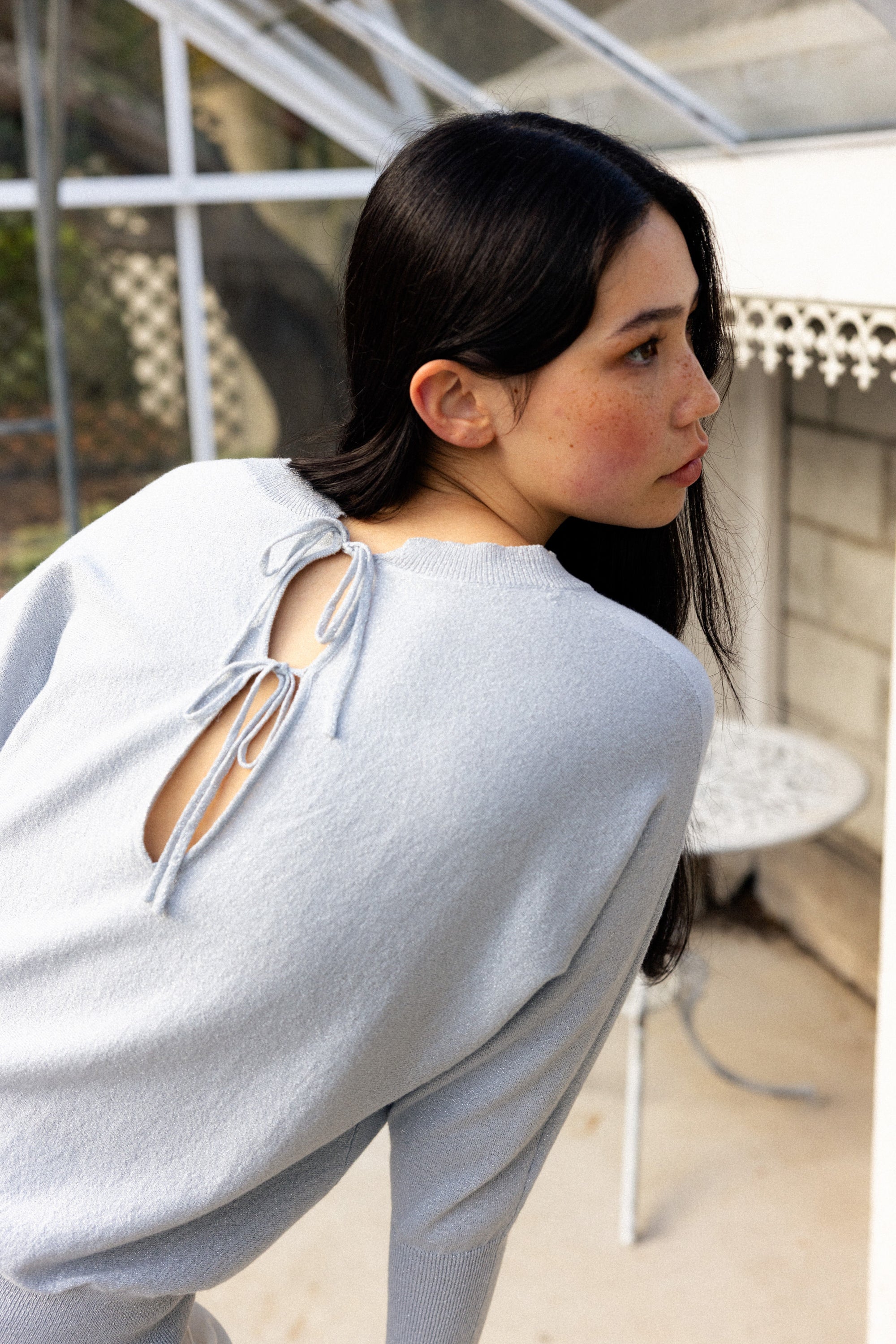 Woman wearing a light gray sweater with cut-out back in an indoor setting.