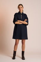 Woman wearing a dark blue dress with black boots on a beige background