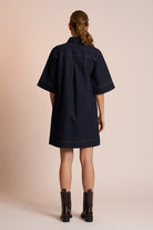 Person wearing a navy dress with short sleeves on a beige background back angle