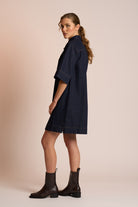 Woman wearing a navy dress and black boots against a beige background side angle