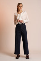 Woman wearing a white blouse and dark pants against a beige background