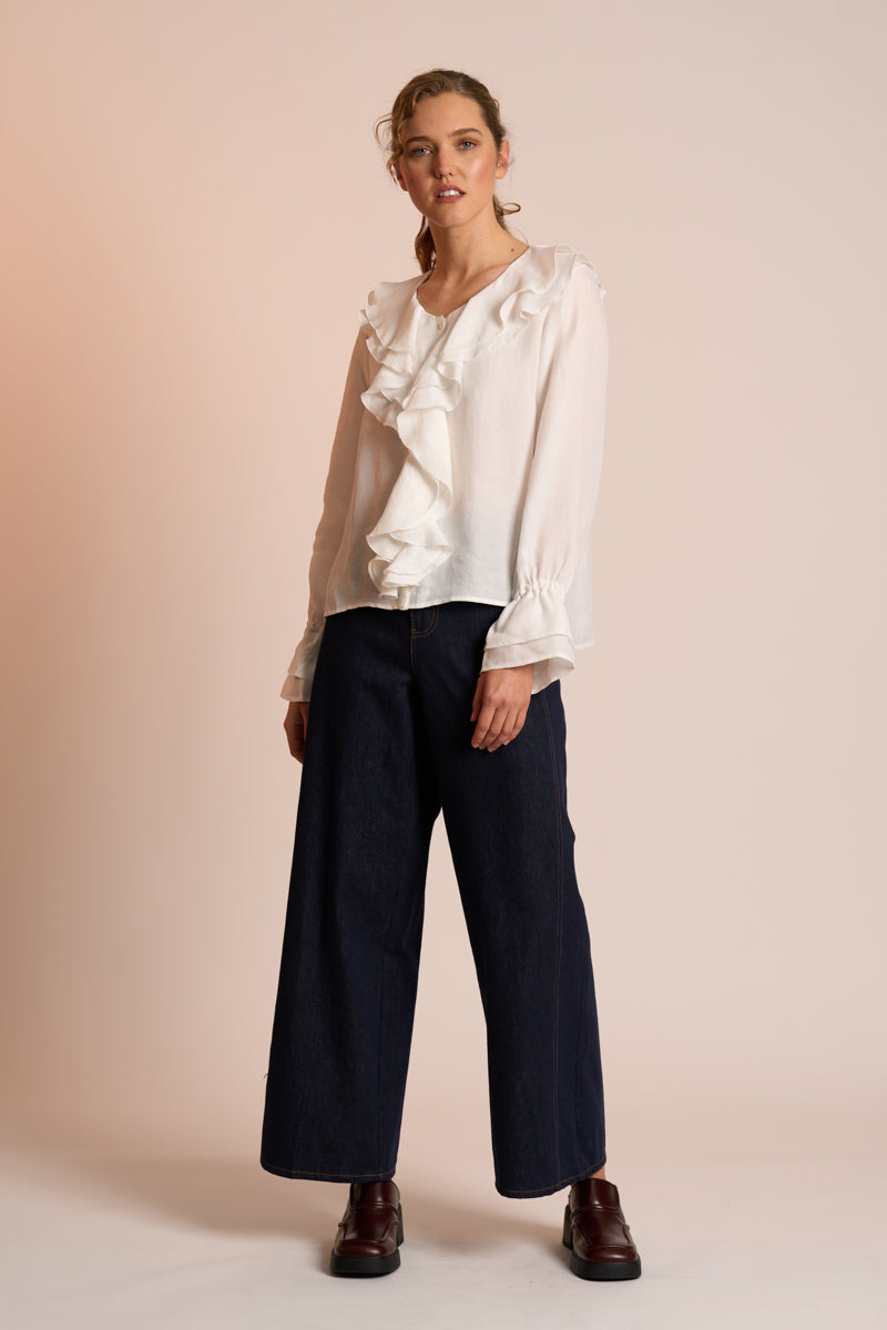 Woman wearing a white blouse with ruffles and dark pants on a beige background