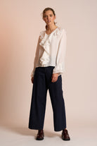 Woman wearing a white blouse with ruffles and dark pants on a beige background