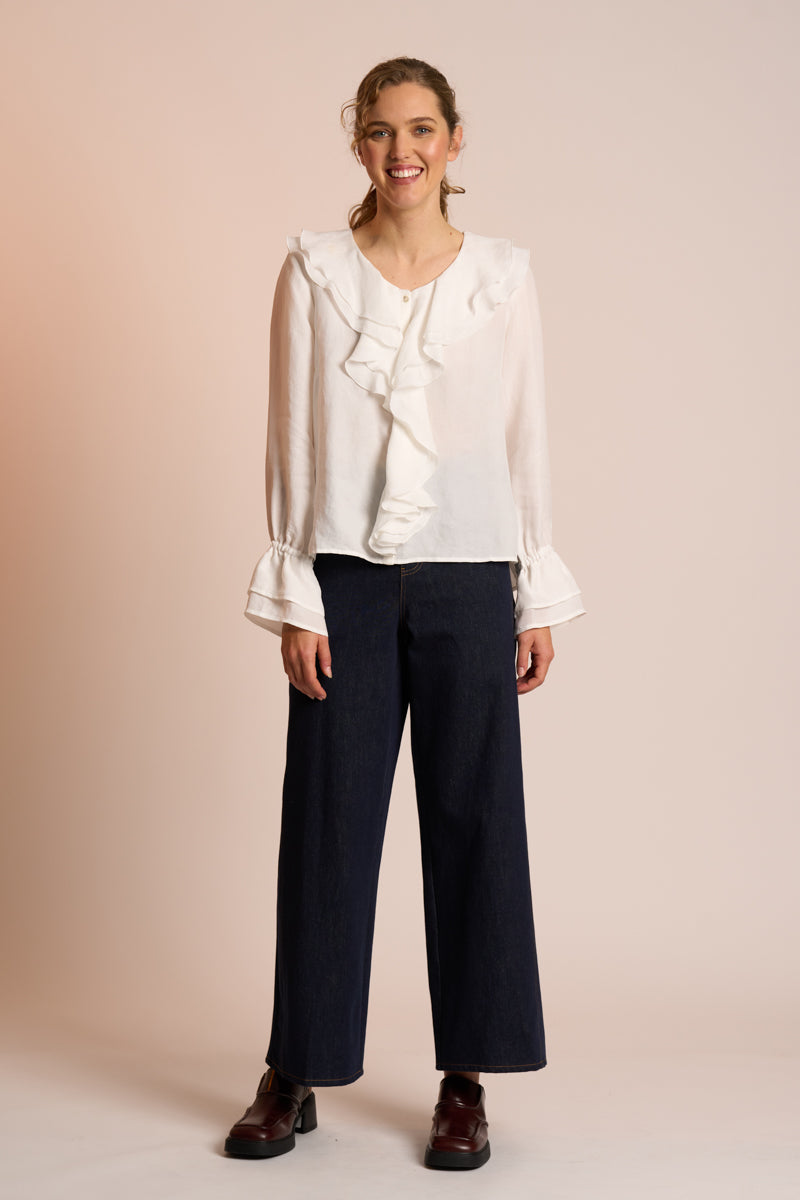 Woman wearing a white blouse with ruffles and dark pants on a beige background