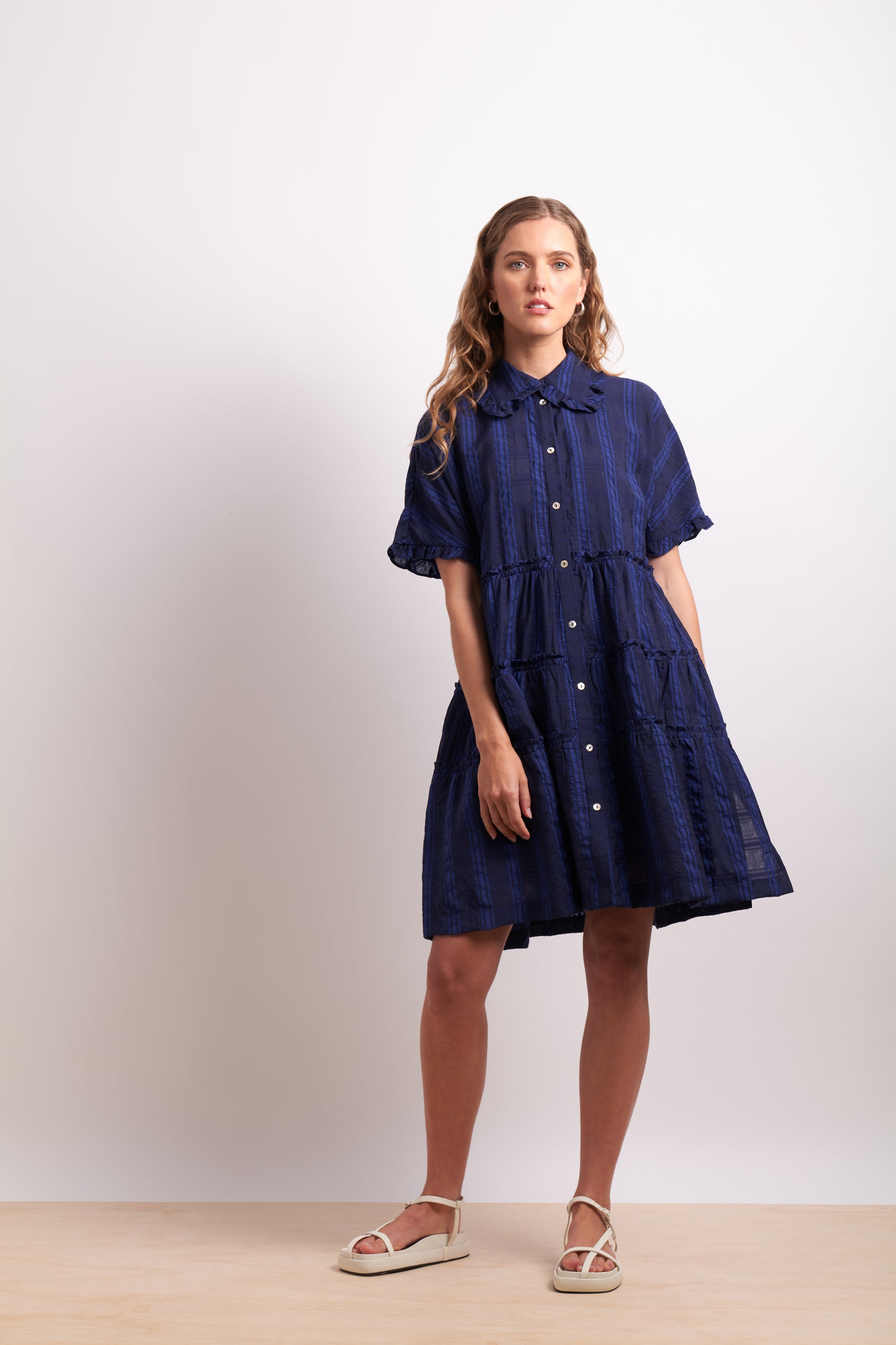 Woman wearing a navy blue dress with white buttons on a plain background