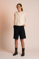 Woman wearing an off white gilet, black shorts, and boots on a beige background